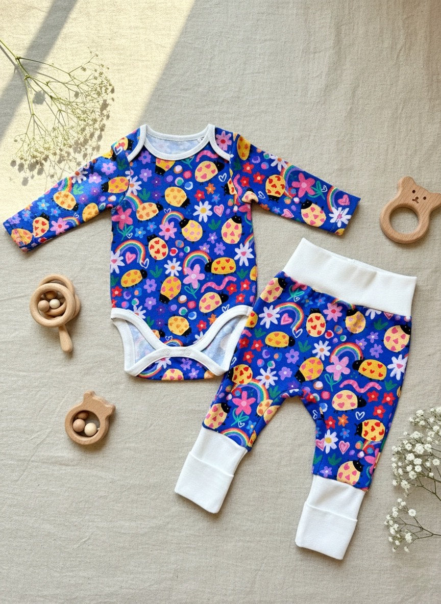 Colorful baby onesie and pants set on a neutral fabric background with wooden toys.